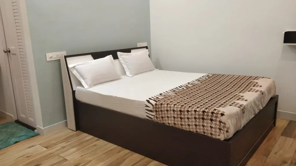 Bright bedroom with wooden bed frame and teal accent rug at Trip Chikmagalur Homestay P3