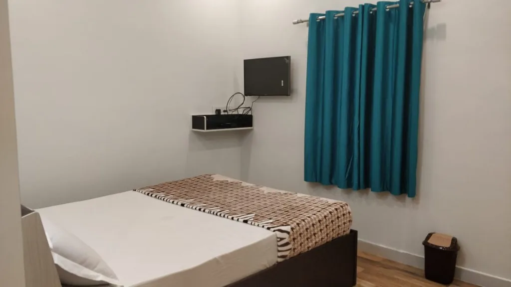 Double bedroom with wall TV, teal curtains and white linens at Trip Chikmagalur Homestay P3