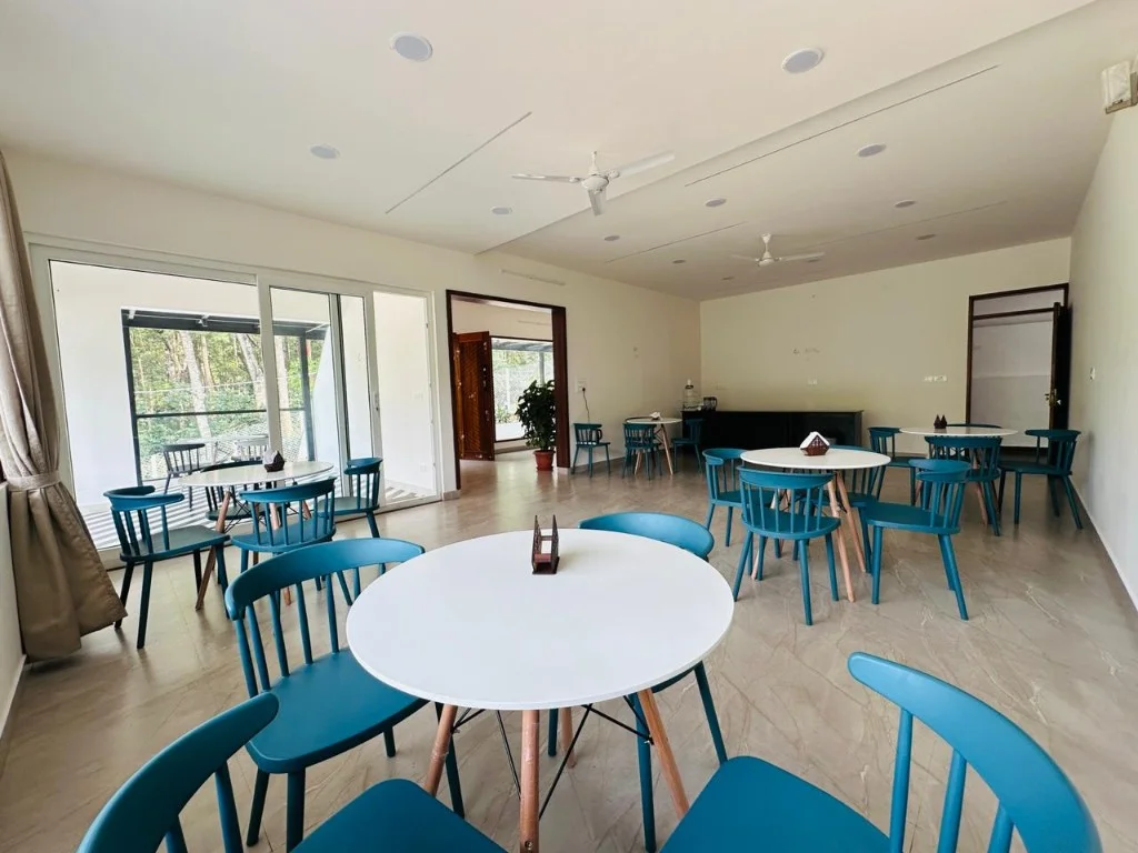 Bright shared dining hall with teal chairs and white tables at Trip Chikmagalur Homestay P3