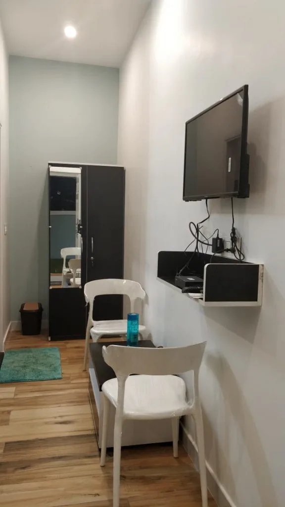 Room lounge area with TV, wardrobe and white chairs at Trip Chikmagalur Homestay P3